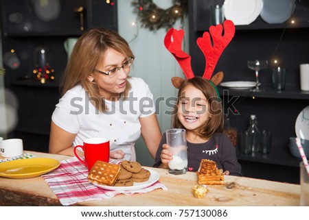 Cute little girl and her mother drinking milk and eating cookies in home Christmas holiday. Christmas family portrait.
