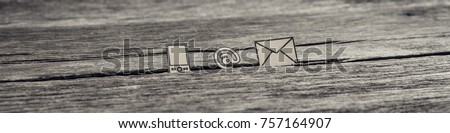 Wide panorama view of at sign, mail and mobile phone icons stuck in between a crack in the wooden surface, toned retro effect.