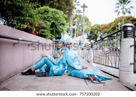 Outdoor portrait of lovely young playful couple with Malay or Asian traditional wedding dress sitting and posing at park. Selective focus