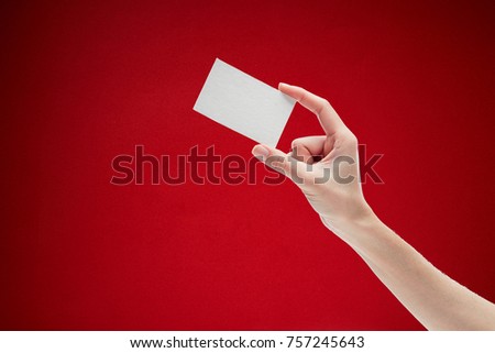 Female hand holding white business card on red background.