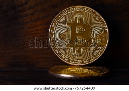 Two new golden physical bitcoins lies on dark wooden backgound, close up. High resolution photo. Cryptocurrency mining concept