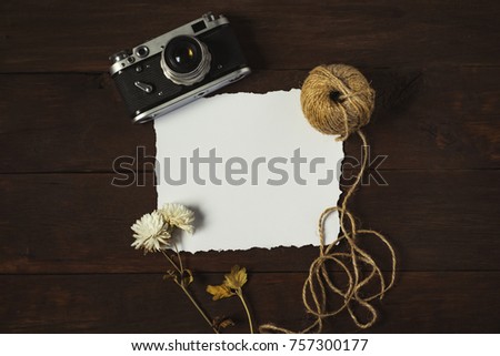 Retro camera, dry flower and tangle of twine yarn on a wooden background. A blank sheet of paper.