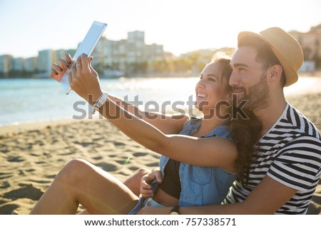 Happy woman taking selfie with her boyfriend by tablet on beach
