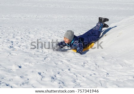 Little happy boy sliding from the snowy hill down in winter day