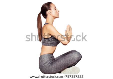 Beautiful smiling young woman in sportswear sits on the floor after a workout and looks at the camera on a white background