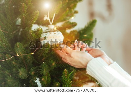 A woman is decorating a Christmas tree. A cozy and joyful evening by the fireplace, lights are shining, the family is gathered.