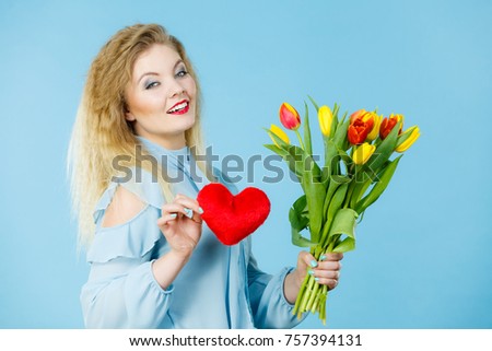 International women or valentine day. Beautiful woman blonde hair fashion make up holding tulips bunch and red heart sign. On blue