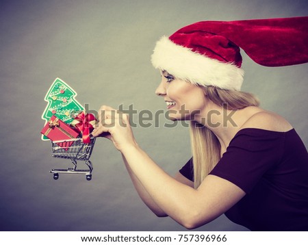 Xmas, seasonal sales, winter celebration concept. Happy woman wearing Santa Claus helper hat holding shopping basket cart with little christmas tree and gifts inside running for sale.