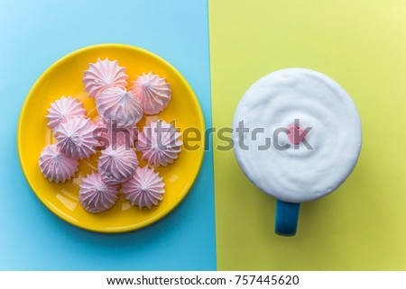 blue  mug with cocoa with whipped cream decorated with heart shaped pink candy  and plate with meringue on a bright background.