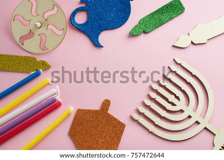 Image of Jewish holiday Hanukkah with wooden dreidel (spinning top) , menorah (traditional Candelabra) candles, children's stickers glitter craft on pink background.Top view.