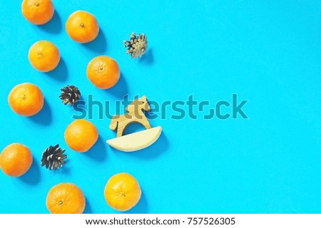 Orange mandarins, a wooden toy horse and pine cones on a blue background. Christmas and New Year decoration. Festive backdrop, mockup for site and gift cards. Winter presents