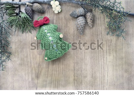 Collection of Christmas ornaments made in crochet, on rustic wooden background framed with mistletoe leaves and pine cone. Top view and copy space