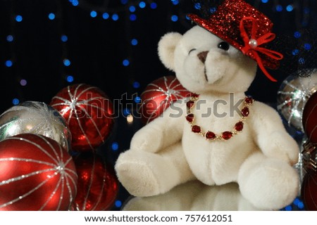 Cute white teddy bear in a red shiny hat, sitting among the glittering balls
