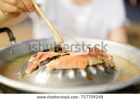 Hand holding chopsticks with squid for grilled on metal stove with pork, beef or chicken and soup - food for winter concept.