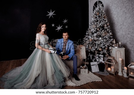 Elegantly dressed man and the woman in the room decorated by Christmas against the background of the Christmas fir-tree exchange gifts.