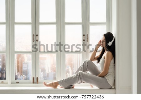 A cute Asian girl is listening a classic song in front of white window in a holiday of weekend . Royalty-Free Stock Photo #757722436