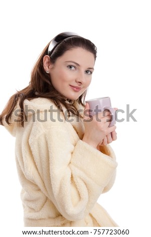 Young attractive woman holding cup of tea, wearing bathrobe, looking at camera, smiling.