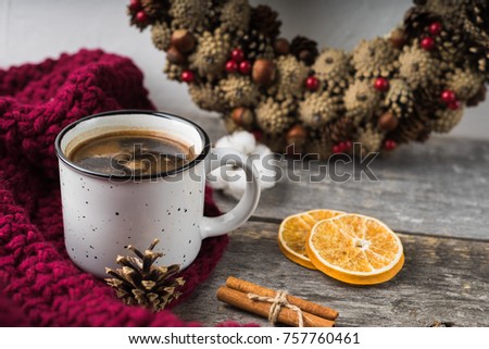 Mug with coffee, orange slices, cinnamon, knitted scarf and wreath of cones on a wooden background. Winter and christmas concept.