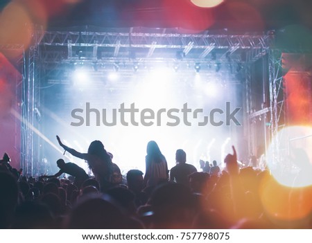 Silhouettes of festival concert crowd in front of bright stage lights. Unrecognizable people and colorful effects.