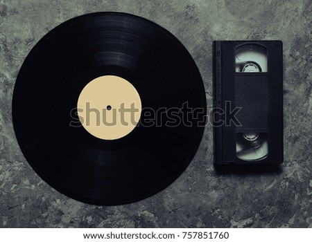 Vinyl plate and video cassette on a gray concrete surface. Retro media technology from the 80s. Top view.