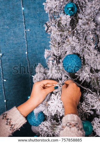 Closeup image of woman in sweater decorating Christmas tree with balls on blue background