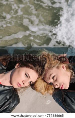 two girls lie touching their heads on the beach. ? girl with ? curly blond hair are looking at a mysterious girl with a straight dark hair 