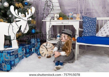 The child, a little girl sitting near a well-dressed Christmas tree and unwraps a gift.