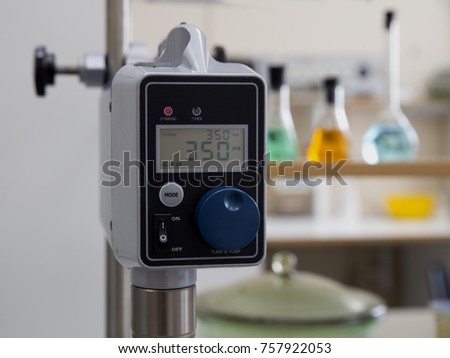 Measurement of solution properties with equipment in chemical laboratory; screen of equipment, indicating numbers, with on the background of flasks with colored liquids 
