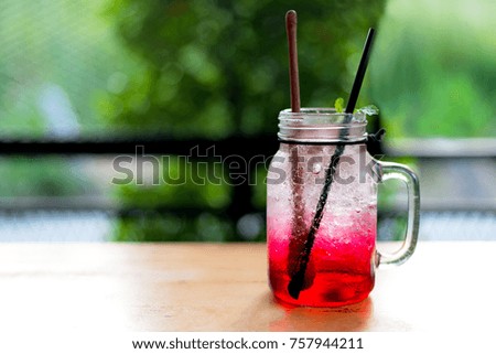 Summer iced fresh drink red juice and cocktail with ice and mint. On wooden table, green nature background, copy space.
