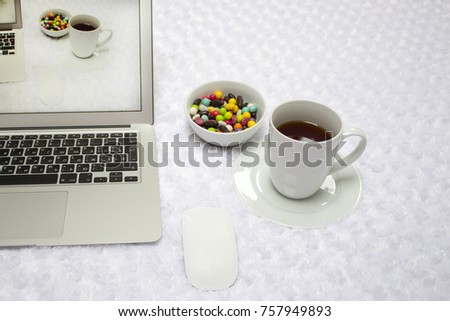 Laptop, a cup of tea, lollipops on a white blanket .  the image on the screen comes to life . duplication shoot. reality and picture on the screen are the same. Concept of escape to real.