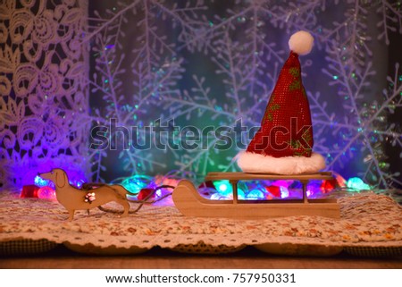 New Year card. Wooden Toys. A dog harnessed to an old village sledge. In the background, a garland of bright colored lights and snowflakes. On the sleigh is a red Santa Claus hat.