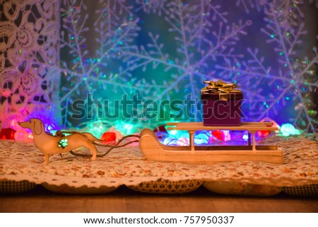 New Year card. Wooden Toys. A dog harnessed to an old village sledge. In the background, a garland of bright colored lights and snowflakes. On the sleigh is a gift box with a gold bow.