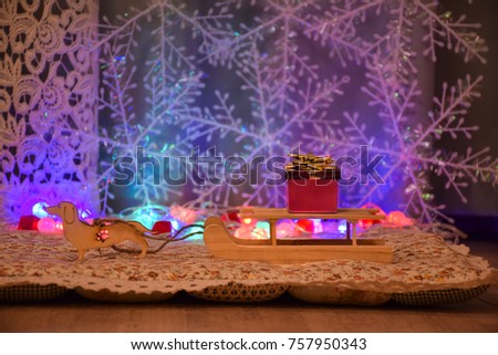 New Year card. Wooden Toys. A dog harnessed to an old village sledge. In the background, a garland of bright colored lights and snowflakes. On the sleigh is a gift box with a gold bow.
