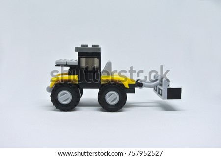 Toy Bulldozer made from yellow and black plastic bricks and with wheels isolated on a white background.