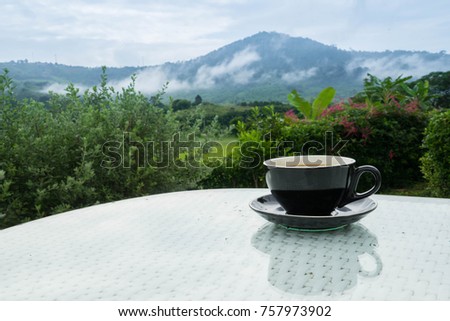 Black coffee cup closeup shot with garden, mountain and fog in the background