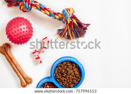 Dry pet food in bowl and toys for dogs on white background top view