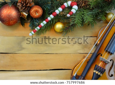 A miniature violin creates a border of artificial pine and holly with Christmas balls and and candy cane on a wooden background. Copy space.