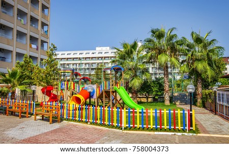 Children's playground near multi-storey house in tropical area with palm trees on sunny summer day.