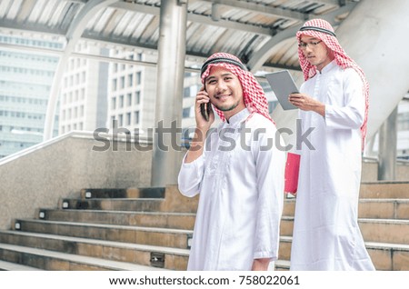 muslim businessman in traditional clothes talking on cell phone and handsome arab business man hold and browsing a digital tablet