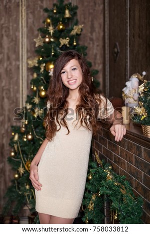 beautiful young girl with open sincere joyful happy smile in retro vintage gold dress standing near fireplace and Christmas tree