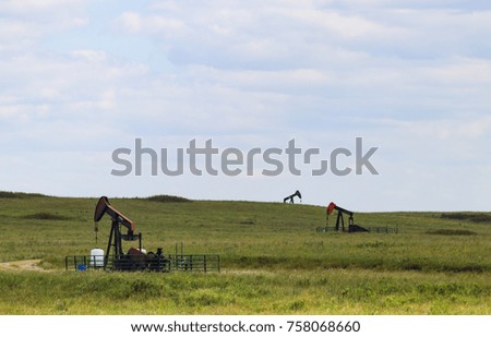 Three working pump jacks on oil or gas wells out in a green field