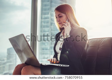 Young woman waiting in a hall sitting in modern office working on laptop talking on the phone Royalty-Free Stock Photo #758070955