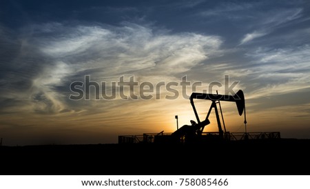 
Silhouette of crude oil pump in oilfield at sunset blue hour.