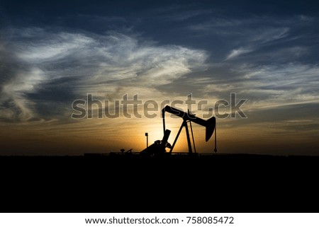 
Silhouette of crude oil pump in oilfield at sunset blue hour.