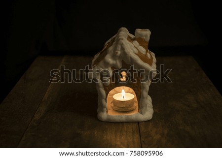 Beautiful gingerbread house with candle standing on wooden table and black background, nice, calm and peaceful image of christmas decoration