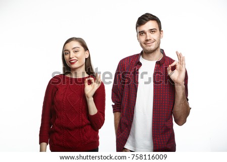 Isolated shot of cute cheerful young couple man and woman advertising some product, making ok gesture as sign of good quality, posing at studio wall. People, goods, advertisment and family concept