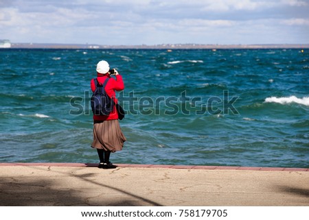 A middle-aged woman photographs the seascape. Embankment, strong wind, waves.
