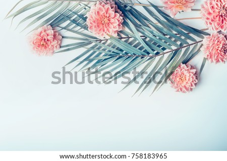 Creative layout with tropical palm leaves and pastel pink flowers on  light turquoise blue desktop background, top view, place for text, horizontal