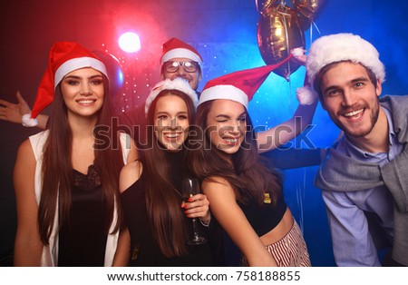 Celebrating New Year together. Group of beautiful young people in Santa hats throwing colorful confetti and looking happy