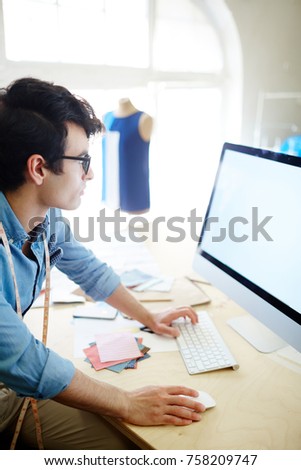 Young designer or tailor looking through fashion trends in computer monitor